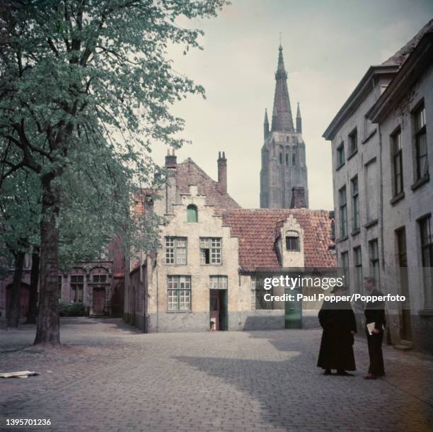 Two men stand and talk on a square lined with old houses in a beguinage complex in the city of Bruges in the West Flanders province of Belgium circa...