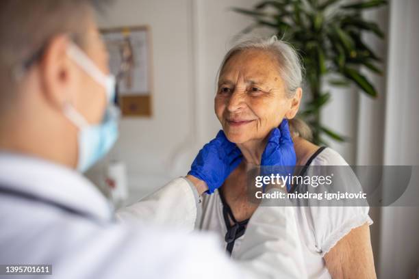 at the office, female doctor examining the senior female patient, while palpating the lymph nodes - schildklier stockfoto's en -beelden