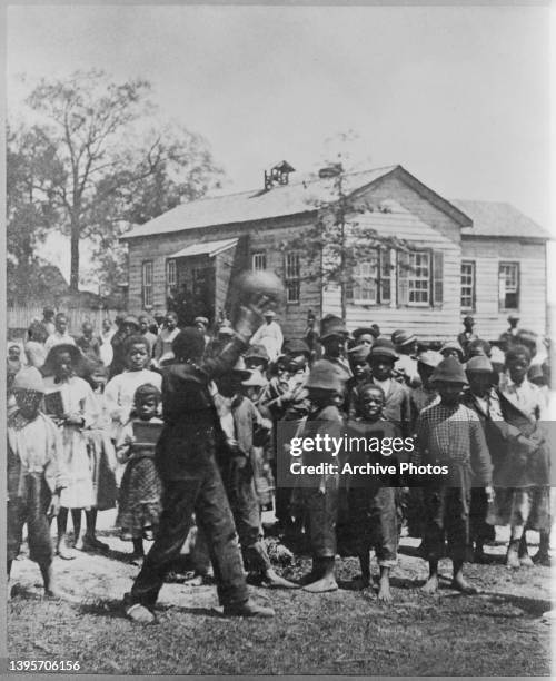 Group of schoolchildren outside during a recess from Miss Schofield's school for freed African Americans, the school building visible in the...