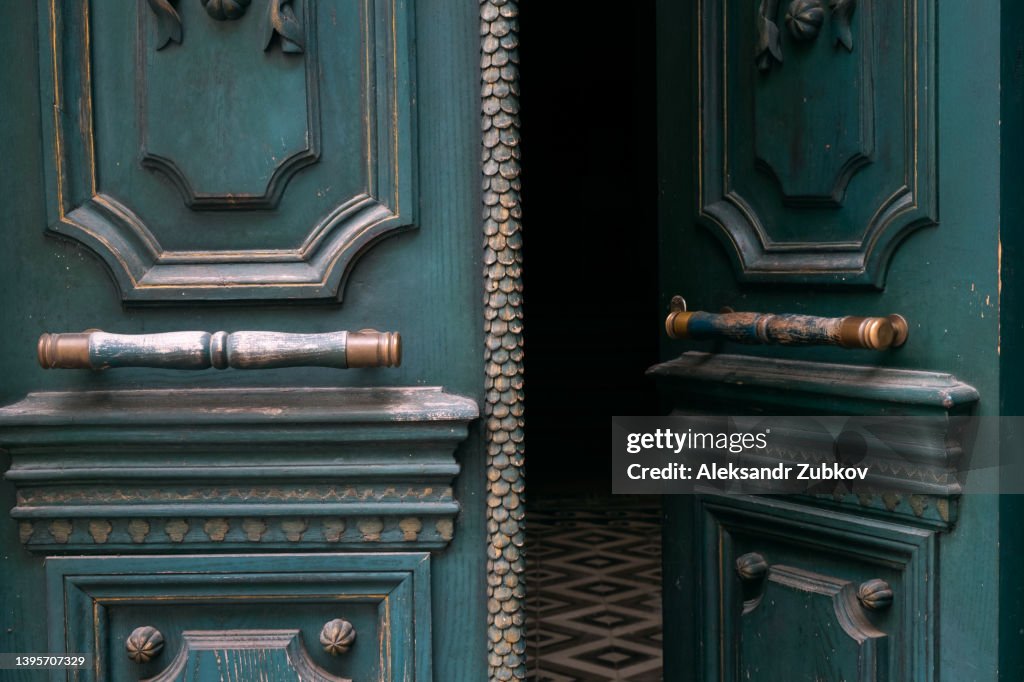 An old worn-out open front door, recently painted, with a bronze or metal wrought iron handle as a background. Door handle close-up. Copy space.