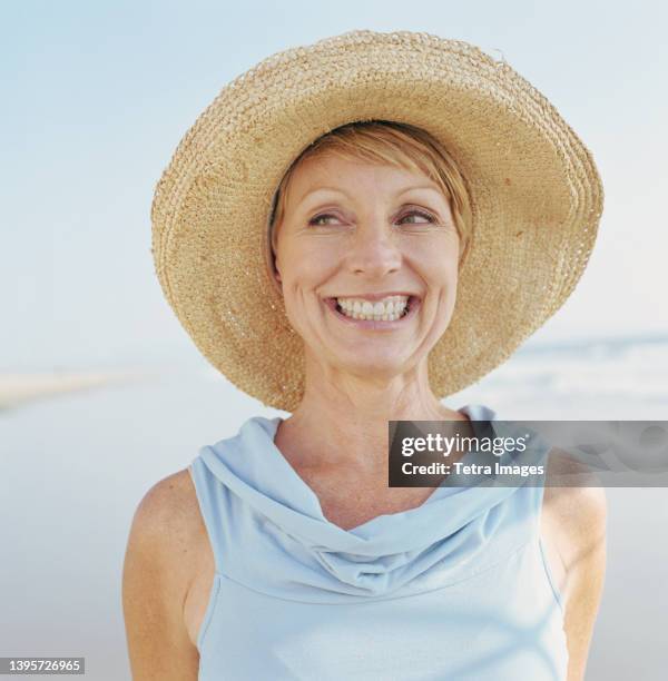 portrait of mature woman wearing hat on beach - strohhut stock-fotos und bilder