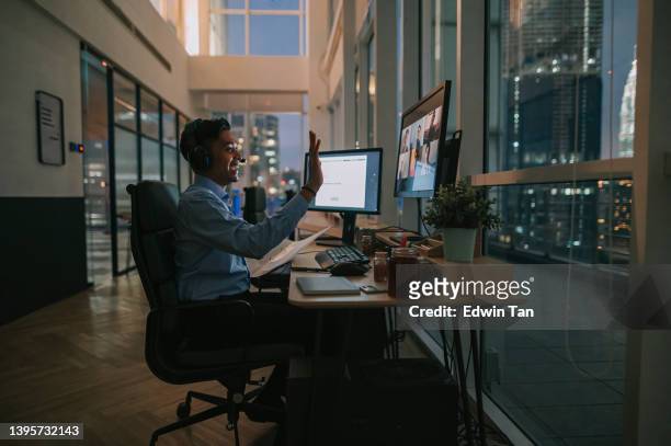 asian indian male white collar worker video call working late in office alone in low light - multiple screens stockfoto's en -beelden