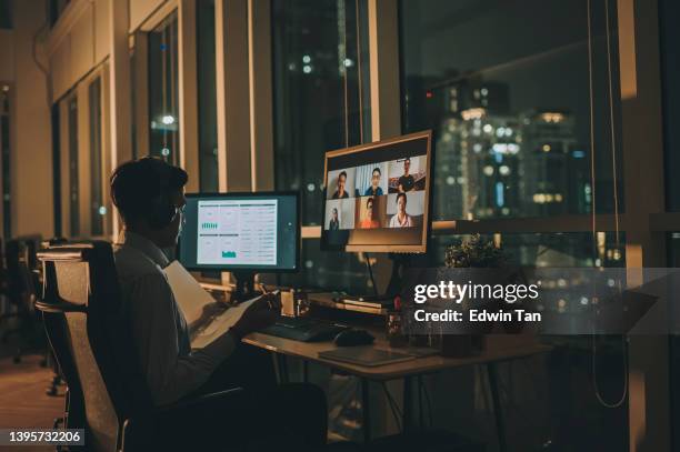 asiatischer indischer männlicher angestellter videoanruf, der spät im büro alleine bei schlechten lichtverhältnissen mit einem ausländischen kollegen arbeitet - 48 hours stock-fotos und bilder