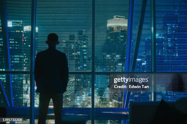 asian chinese businessman in silhouette rear view looking at city at night with blue illuminated city light - man silhouette back lit stock pictures, royalty-free photos & images