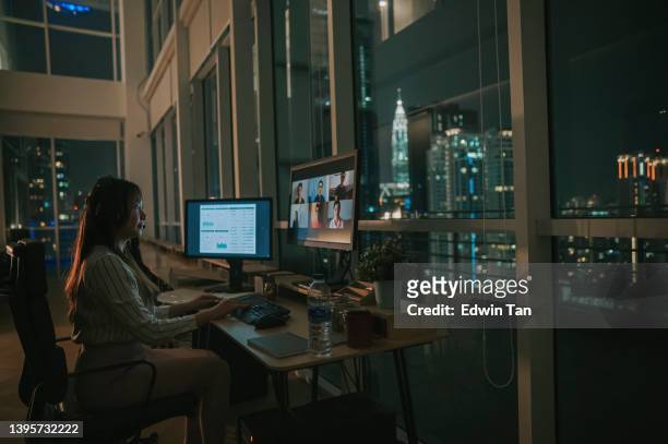 asiatische chinesische arbeiterin videoanruf, die spät im büro alleine bei schlechten lichtverhältnissen arbeitet - schwache beleuchtung stock-fotos und bilder