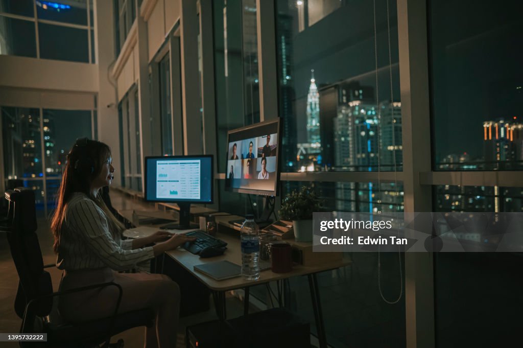 Asian Chinese female white collar worker video call working late in office alone in low light