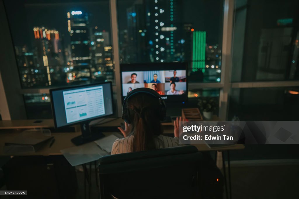 Asiatische chinesische Arbeiterin Videoanruf, die spät im Büro alleine bei schlechten Lichtverhältnissen arbeitet