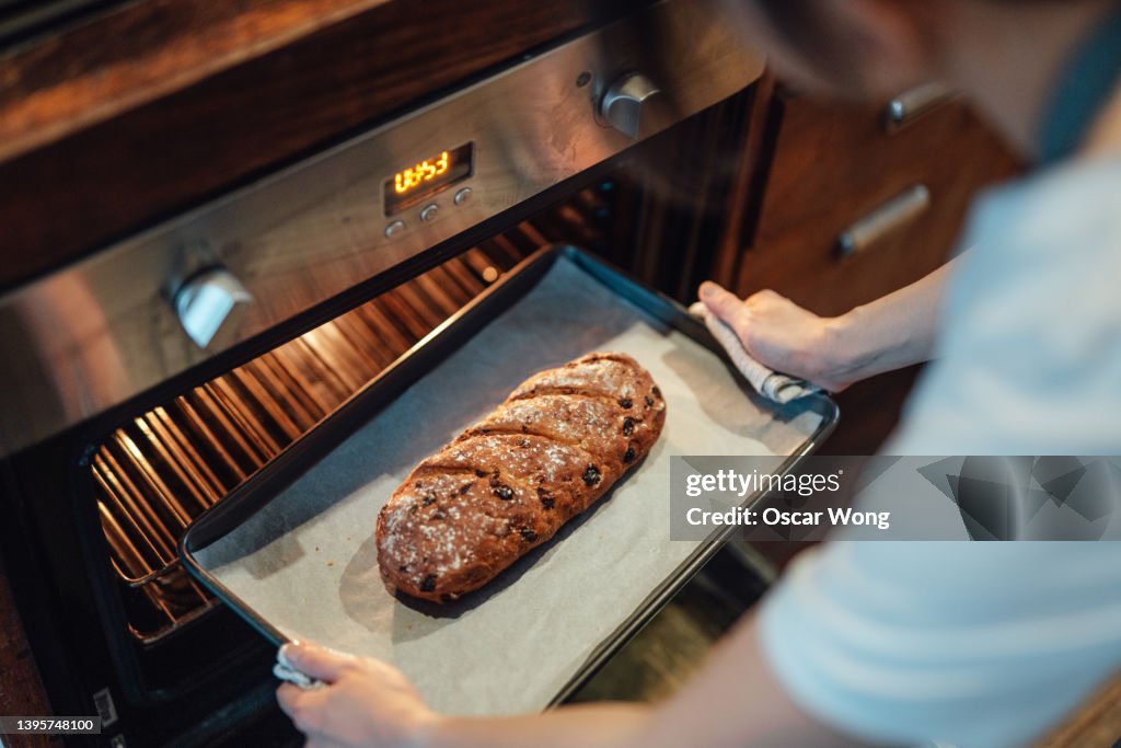 Over the shoulder view of female baker taking out a homemade baked bread with a baking tray fresh from the oven