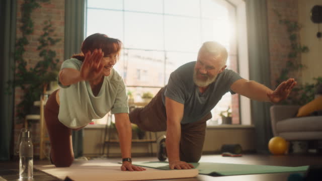 Portrait of a Senior Couple Doing Gymnastics and Yoga Stretching Exercises Together at Home on Sunny Morning. Concept of Healthy Lifestyle, Fitness, Recreation, Couple Goals, Wellbeing and Retirement.