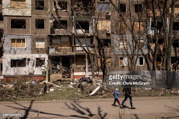 Woman and her child walk past a residential apartment block damaged one day before by a Russian missile strike on May 06, 2022 in Kramatorsk,...
