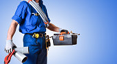 Detail of uniformed plumber with tools and blue isolated background