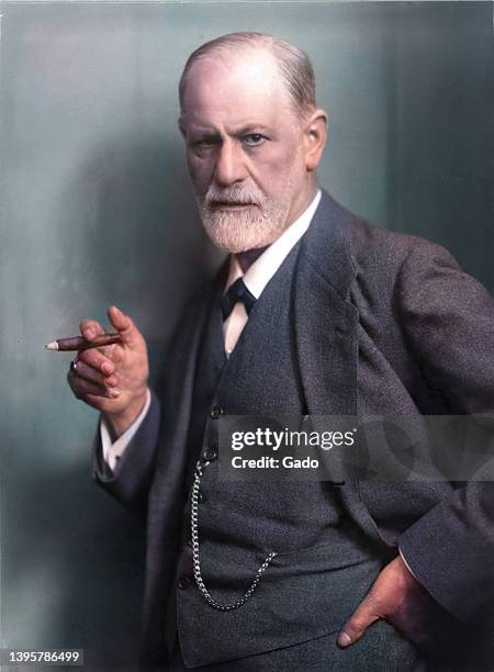 Colorized profile shot of Austrian Neurologist and Psychoanalyst Sigmund Freud, from the waist up, wearing a dark suit and tie and holding a cigar,...