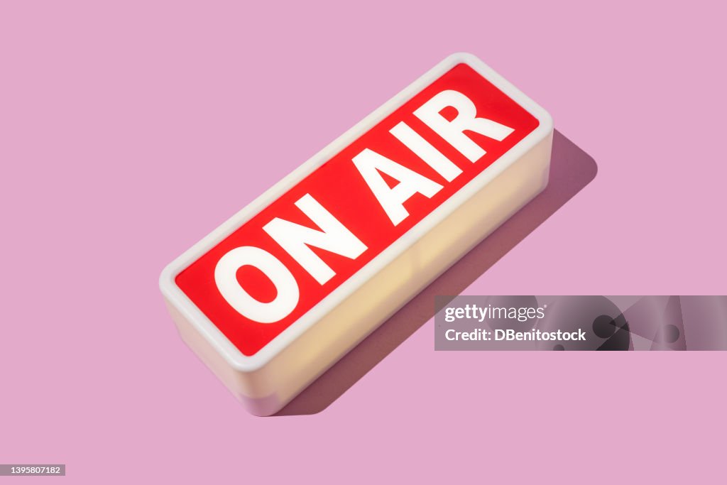 Radio and sound recording warning light that reads: 'ON AIR' with hard shadow on pink background. Podcast, radio, broadcast, radio show, entertainment and journalism concept.