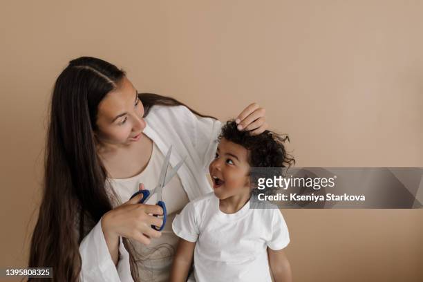 young asian woman cuts her little dark-skinned son with an afro hairstyle in a white t-shirt - dark skin stock pictures, royalty-free photos & images