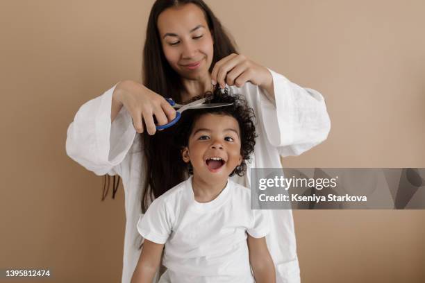 young asian woman cuts her little dark-skinned son with an afro hairstyle in a white t-shirt - dark skin stock pictures, royalty-free photos & images