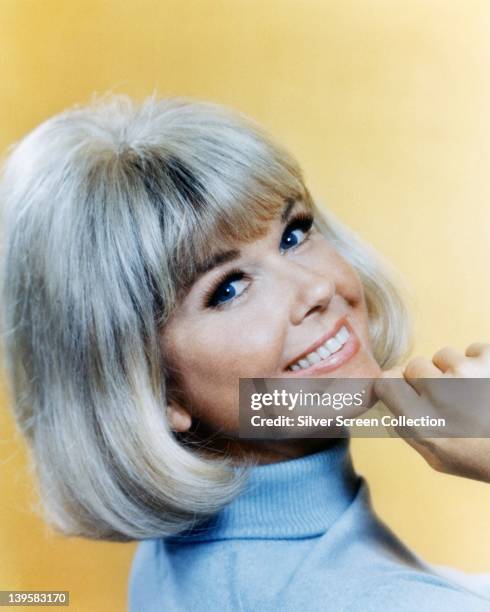 Doris Day, US actress and singer, wearing a light blue polo neck jumper, smiling with her chin resting on her right hand, in a studio portrait,...