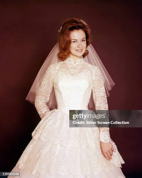 Shelley Fabares, US actress, wearing a white wedding dress, in a studio portrait, against a dark red background, circa 1965.