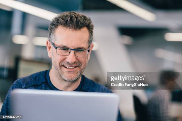 mature caucasian man working on laptop in technology office making video conference call - casual businessman glasses white shirt stock pictures, royalty-free photos & images