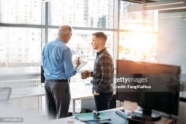 senior colleague mentoring and explaining to young office worker in business company office - cheftrainer stockfoto's en -beelden