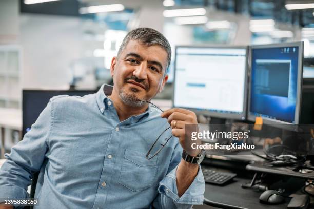 asian middle eastern businessman sitting in office with eyeglasses and computer terminal - grey shirt stock pictures, royalty-free photos & images