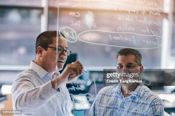 two business colleagues discussing strategy brainstorming on glass board in office - return on investment stock pictures, royalty-free photos & images