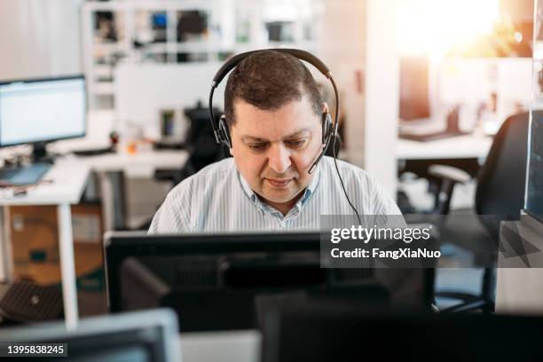 middle eastern businessman working in office computer terminal with headset - eastern european descent stockfoto's en -beelden