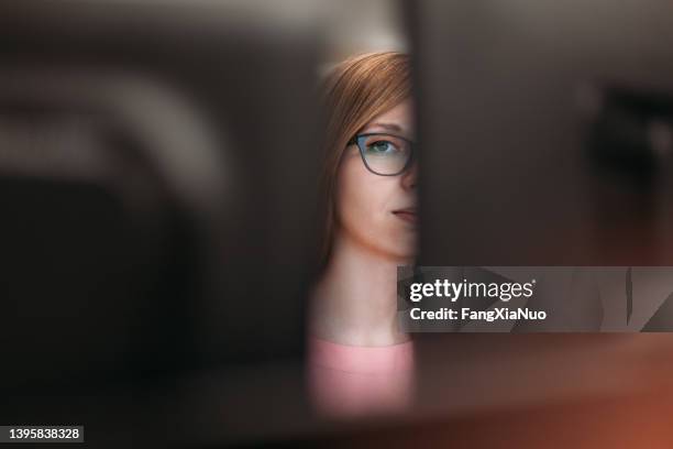 woman peeking through computer monitors in office - bad colleague stock pictures, royalty-free photos & images