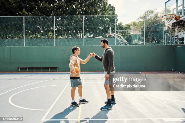 father and son playing a game of basketball. young man and teenage boy having fun, giving a fist bump while staying fit, active - mature men playing basketball stock pictures, royalty-free photos & images