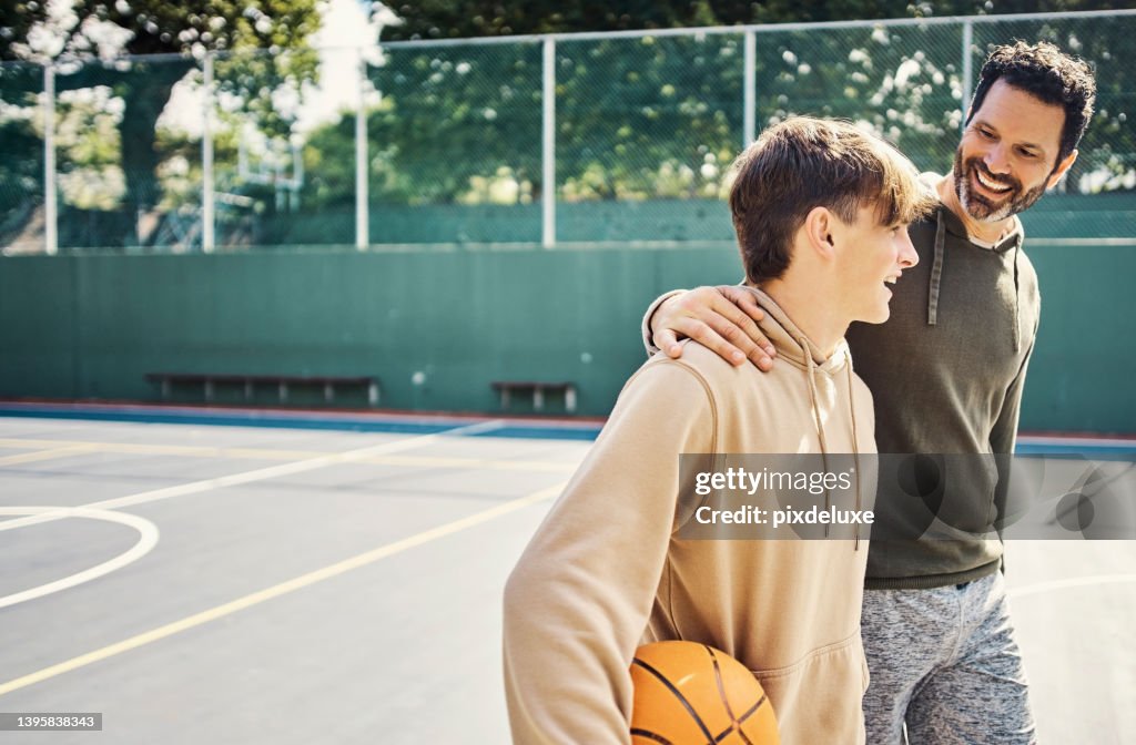 Vater und Sohn gehen nach einer Partie Basketball. Junger Mann und Teenager haben Spaß, reden und plaudern, während sie fit und aktiv bleiben