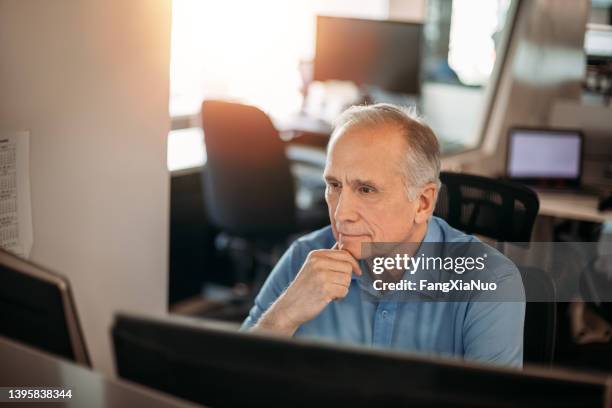 senior businessman contemplating data on computer screen while smiling to make decisions in office - older man computer stock pictures, royalty-free photos & images