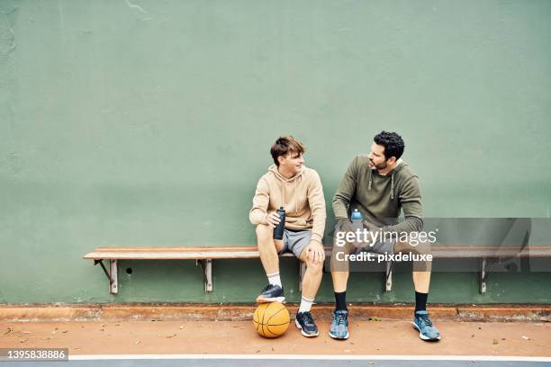 padre e hijo tomando un descanso después de jugar un partido de baloncesto. joven y adolescente hablando y bebiendo agua - banco de jogadores fotografías e imágenes de stock