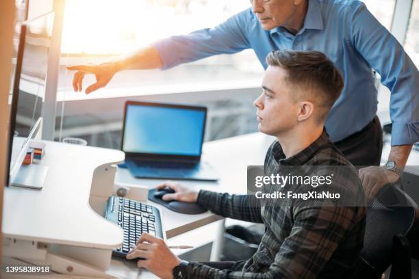 colega que asesora a un asociado más joven en la oficina de negocios mientras señala los datos en el monitor de la computadora - aprendiz fotografías e imágenes de stock