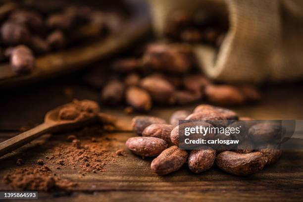 heap of cocoa beans on a rustic wooden table - bean stockfoto's en -beelden