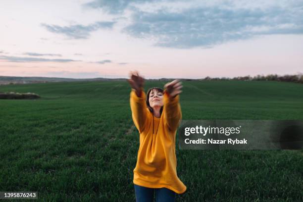 a beautiful woman in a yellow sweatshirt falls down to the green agricultural field - vlag plaatsen stockfoto's en -beelden