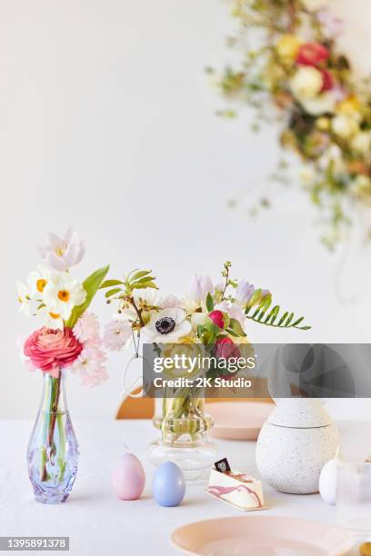 a modern table decoration as an easter table with a floral easter wreath hanging on the wall - easter decoration home stock pictures, royalty-free photos & images