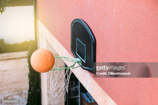 basketball hoop on top of a garage door in a house with the sun in the background, with the ball hitting the hoop. concept of sport, basketball, lifestyle, playing and having fun. - basket sport stock pictures, royalty-free photos & images