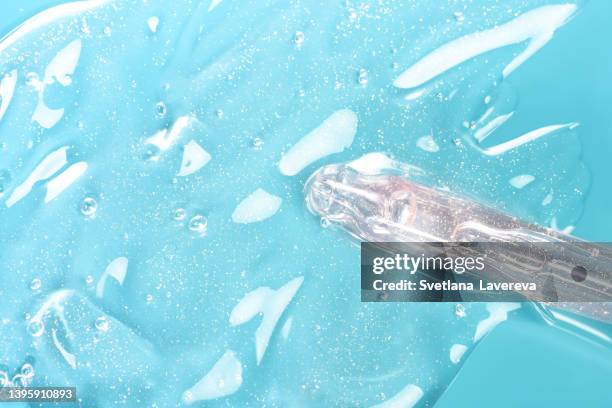 the end of pipette from cosmetic glass dropper with serum or hyaluronic acid or essential oil on the blue background. - cosmetic testing store stock pictures, royalty-free photos & images
