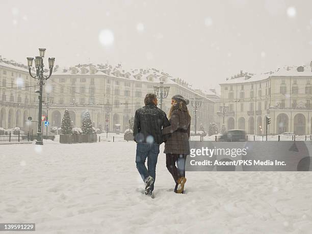 couple walk through urban piazza during snowstorm - italy winter stock pictures, royalty-free photos & images