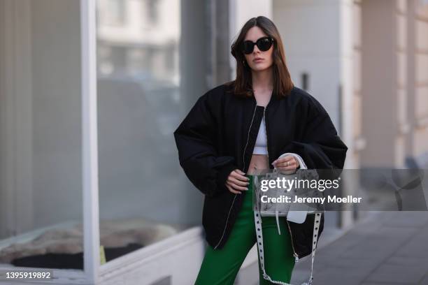 Karla Jenders seen wearing black sunglasses from Prada, a white cropped top from H&M, a black bomber jacket from The Frankie Shop, a green leather...