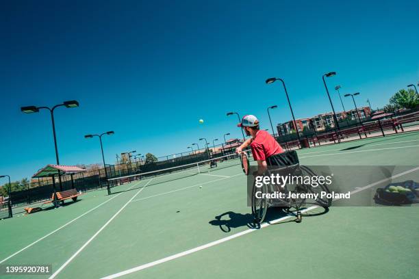 action shot of a handsome young man in a wheelchair serving a tennis ball for adaptive exercise outdoors in the summer - wheelchair tennis stock pictures, royalty-free photos & images