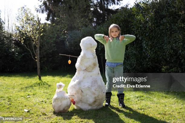 girl (8-9) making a thumbs down gesture whilst standing next to a melting snowman on a sunny spring day in a back yard. - melting snowman stock pictures, royalty-free photos & images