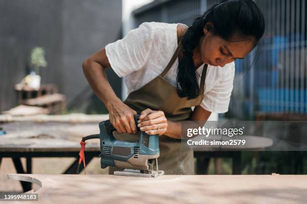 attractive young asian female carpenter using some power tools for her work at a woodshop - woman sleep stockfoto's en -beelden