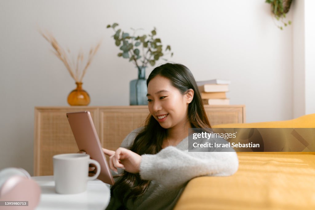 Smiling chinese woman using a digital tablet while sitting on the floor in the living room at home.
