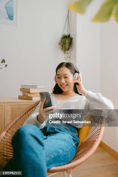 smiling young asian woman having a video call on her mobile phone in her living room at home. - talk phone flat imagens e fotografias de stock