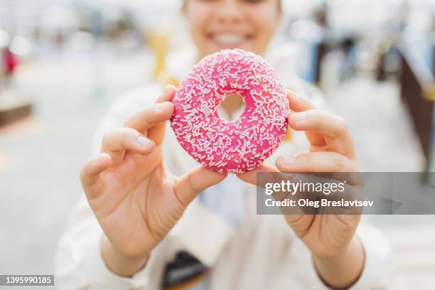 unrecognizable woman holding fresh sweet glazed donut in hands. unhealthy eating with lot of sugar - buñuelo en forma de rosca fotografías e imágenes de stock