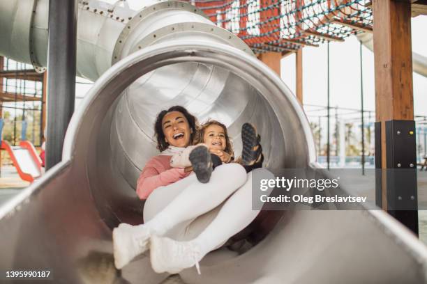 young happy mother with her daughter having fun in tube slide on playground. happy childhood and motherhood - tube girl bildbanksfoton och bilder