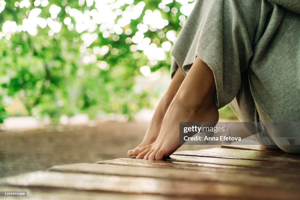 Bare feet of a woman sitting on a wooden bench. She is resting at a public park. Concept of unity with nature