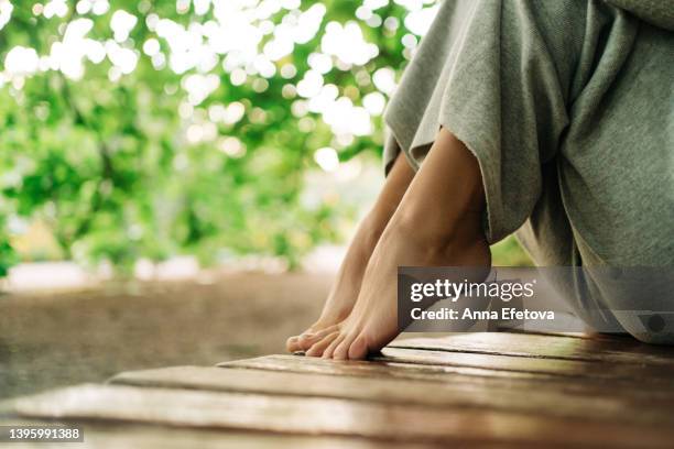 bare feet of a woman sitting on a wooden bench. she is resting at a public park. concept of unity with nature - foot nature green stock pictures, royalty-free photos & images