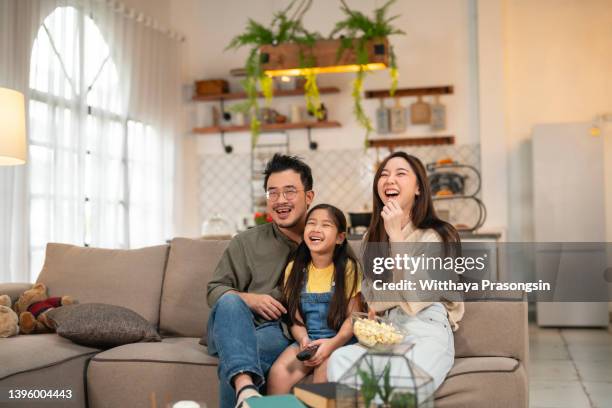 family watching tv and eating popcorn at home - asian family watching tv happy stock pictures, royalty-free photos & images