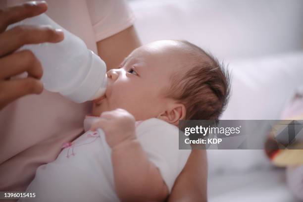mother feeding baby with milk bottle on armchair in the bedroom. - garrafa de leite imagens e fotografias de stock